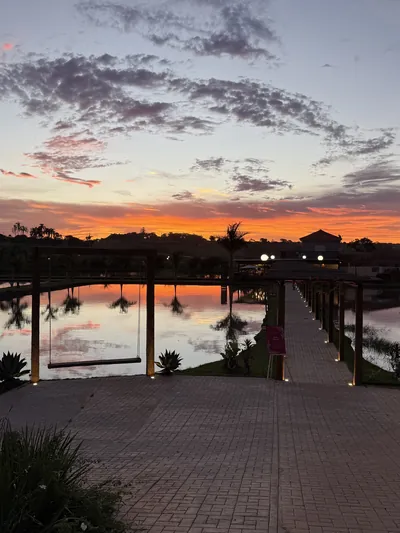 Pôr do sol alaranjado refletido no tanque, com o píer iluminado e o balanço